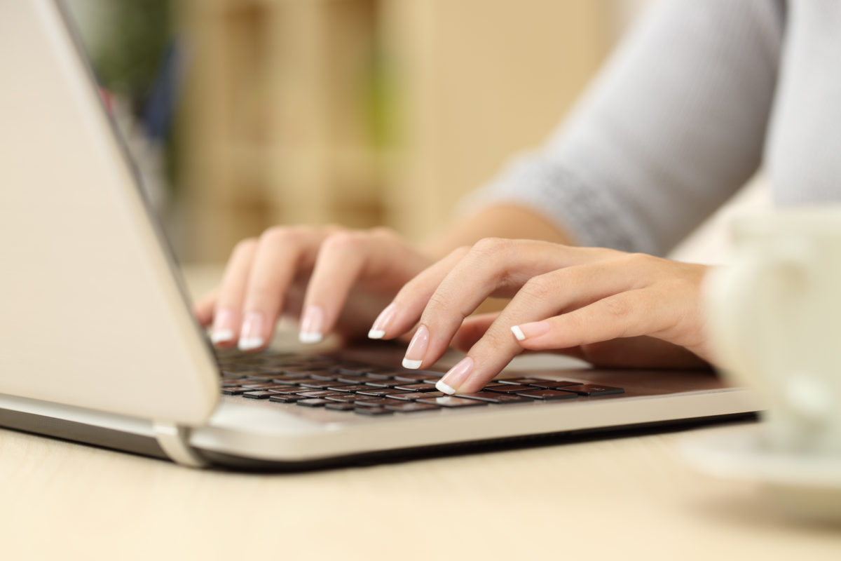 Person with a French manicure typing on a Macbook laptop.